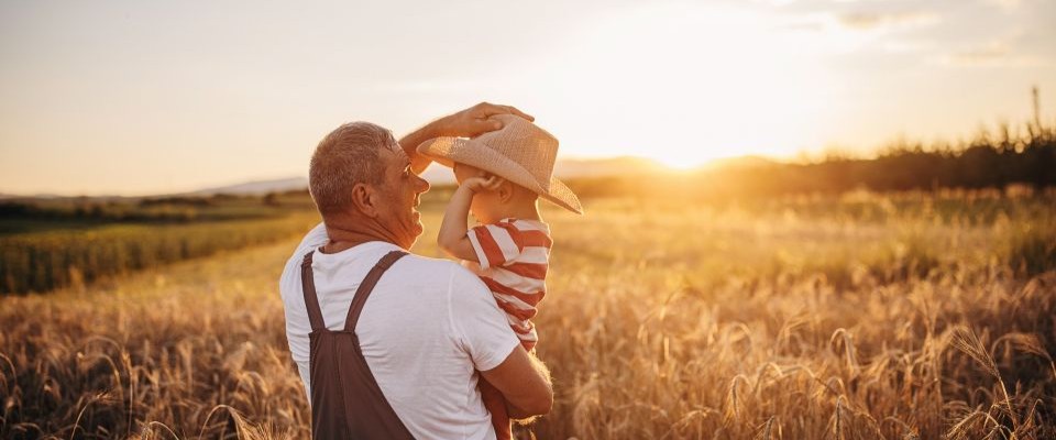 Man holding child wearing cowboy hat in a field